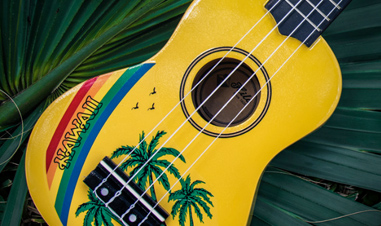 yellow ukulele with Hawaiian design on top of palm branch