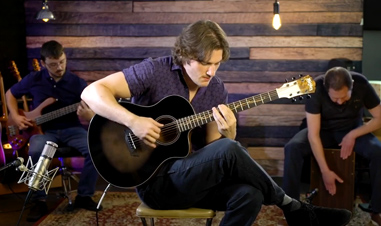 man playing Washburn acoustic guitar in front of man playing electric bass and man playing cajon
