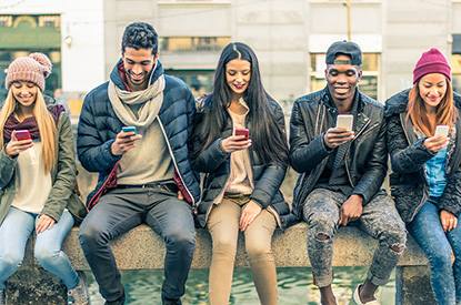 five young adults on a bench on using phones